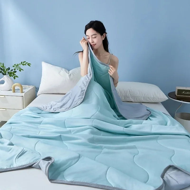 A light blue quilted blanket draped over a bed in a softly lit room.