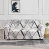 A white stretch floral elastic sofa cover displayed on a light gray floor with framed artwork in the background.