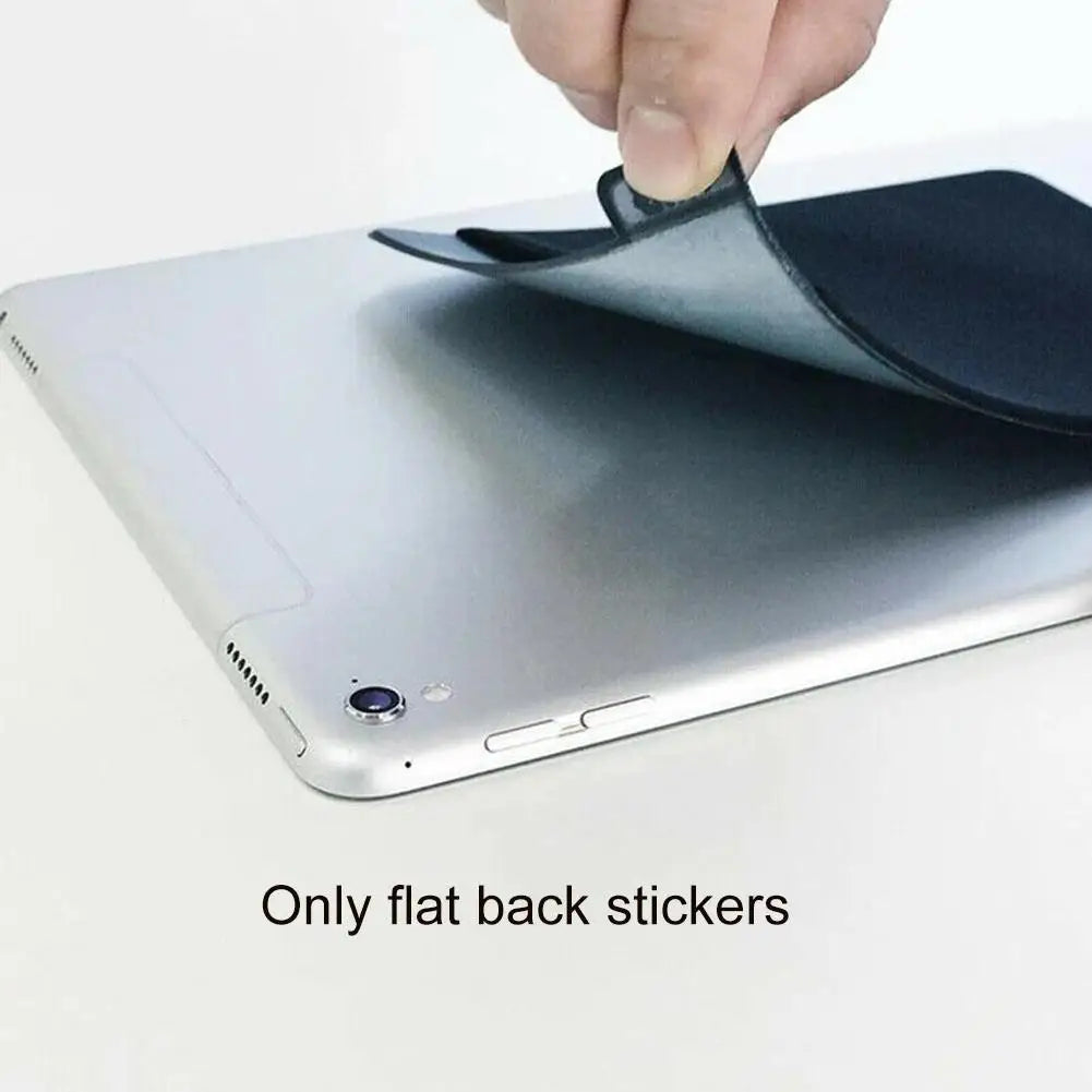 A hand is placing a black flat sticker onto the silver back of a laptop.