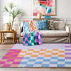 A colorful retro checkerboard geometric rug laid on a wooden floor in front of a sofa.