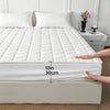 A white quilted mattress protector is shown on a bed, highlighting its 12-inch thickness.