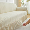 A cream-colored jacquard stretch sofa cover is being fitted onto a light-colored sofa.