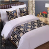 A close-up of a bed decorated with gold patterned fabric pillows and bedding against a gray wall.