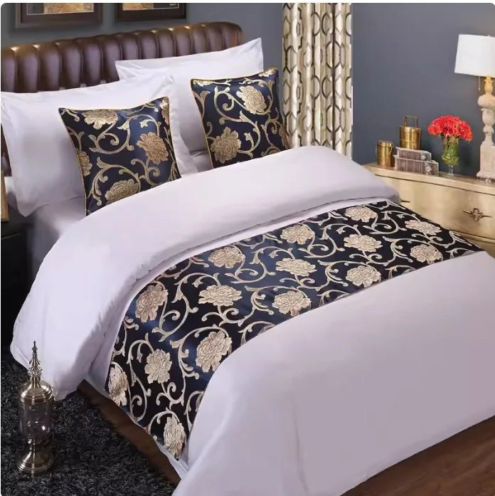 A close-up of a bed decorated with gold patterned fabric pillows and bedding against a gray wall.