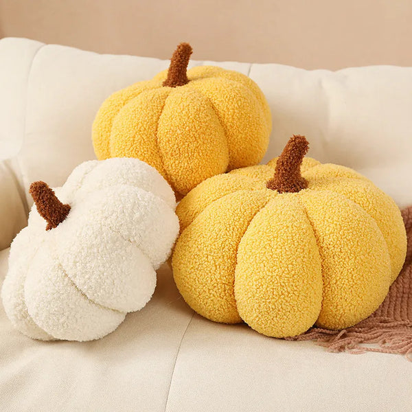 A set of plush pumpkin throw pillows in yellow and white textures resting on a light-colored sofa.