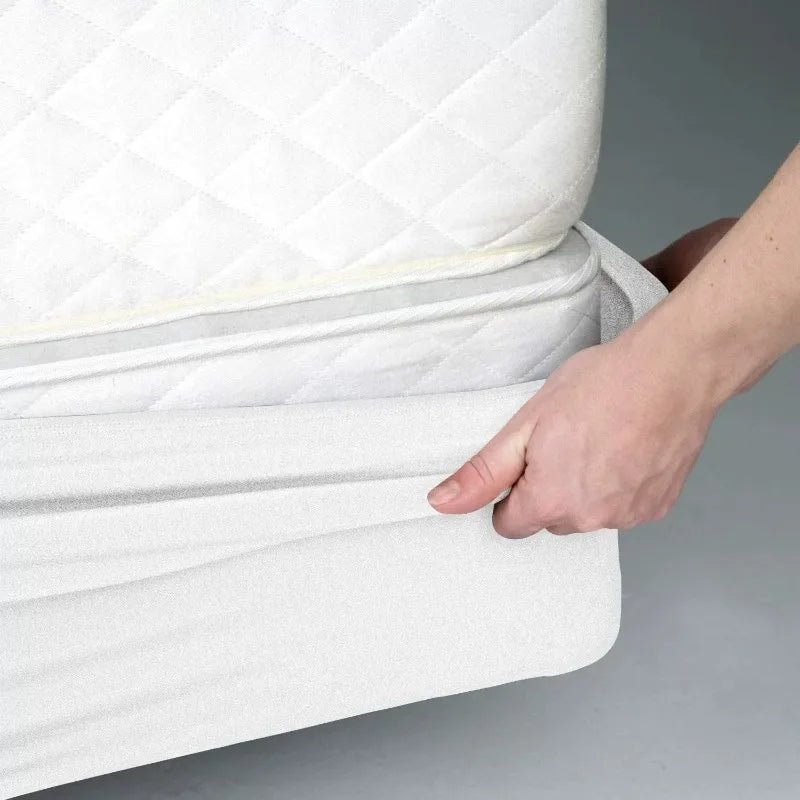 A hand is adjusting a white quilted box spring protector cover on a mattress.
