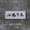 A rectangular white embroidered badge with black Chinese characters on a dark gray textured background.