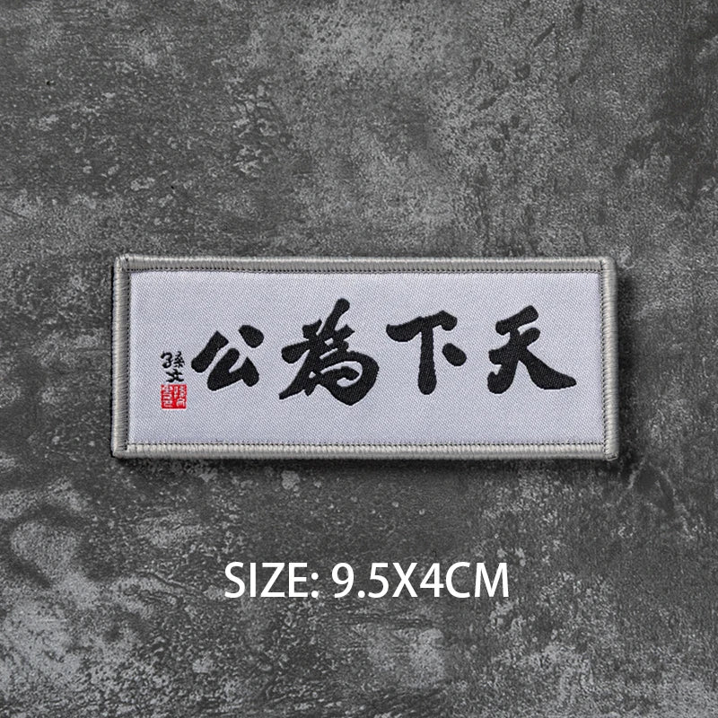 A rectangular white embroidered badge with black Chinese characters on a dark gray textured background.