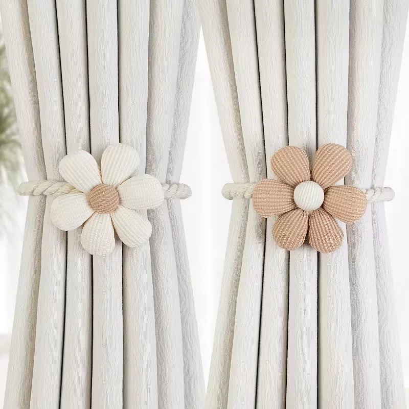 A pair of beige magnetic floral curtain tiebacks attached to white fabric curtains.