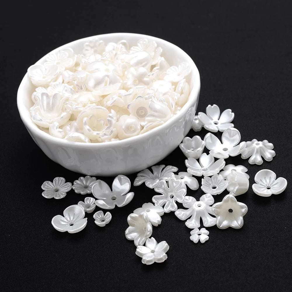 A white bowl filled with imitation pearl flower spacer beads, with loose beads scattered beside it.
