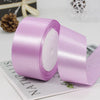 Roll of light purple satin craft ribbon with decorative trim shown on a white surface.