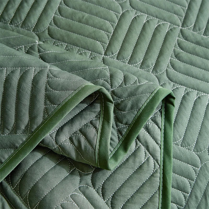 A close-up of a sage green quilted fabric, likely bedding or a quilt, showing the stitching and folds.
