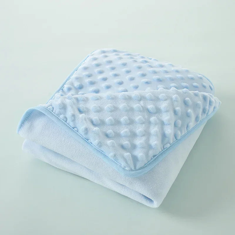 A soft light blue fleece swaddle blanket with a dimpled texture folded neatly on a light surface.