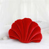 A bright red velvet stuffed sofa cushion shaped like a decorative seashell, resting on white fabric.