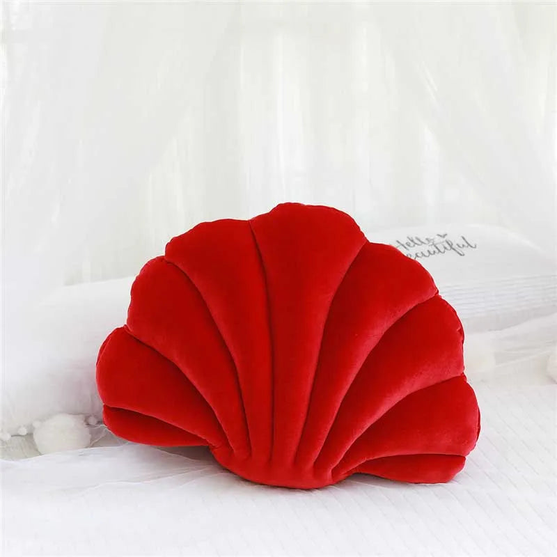 A bright red velvet stuffed sofa cushion shaped like a decorative seashell, resting on white fabric.