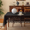 Elegant black lace tablecloth with floral embroidery covering a dark wooden table.