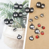 A collection of black and silver ladybug resin charms displayed on a brown card next to green foliage.