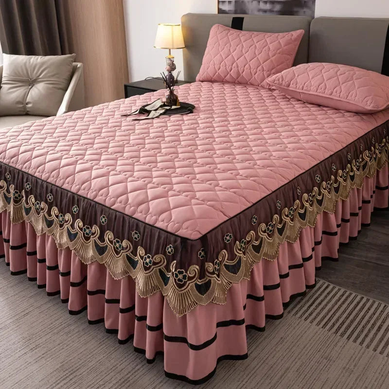 Pink quilted bed skirt with gold embroidery and ruffled hem on a bed.