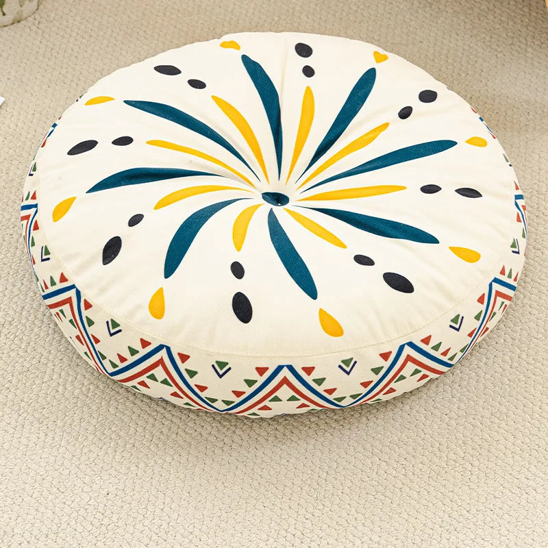 A round cushion with a white background featuring blue, yellow, and black petal-like patterns and a colorful geometric border