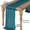 A teal semi-sheer gauze table runner draped over a wooden table, showing its length and texture.