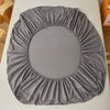 A gray fitted sheet with elastic edges is shown lying flat on a white surface.