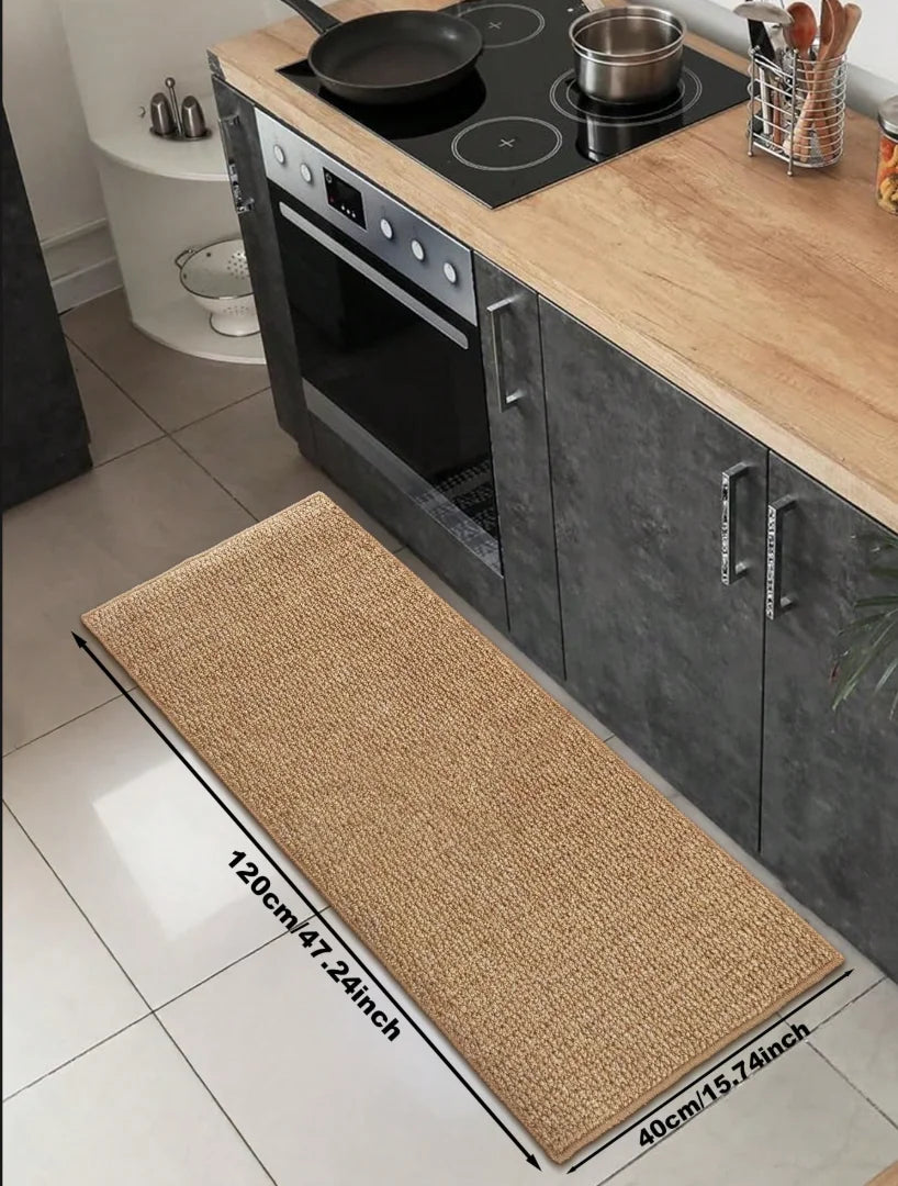 A rectangular woven kitchen runner mat placed on a tiled floor next to a stove and oven.