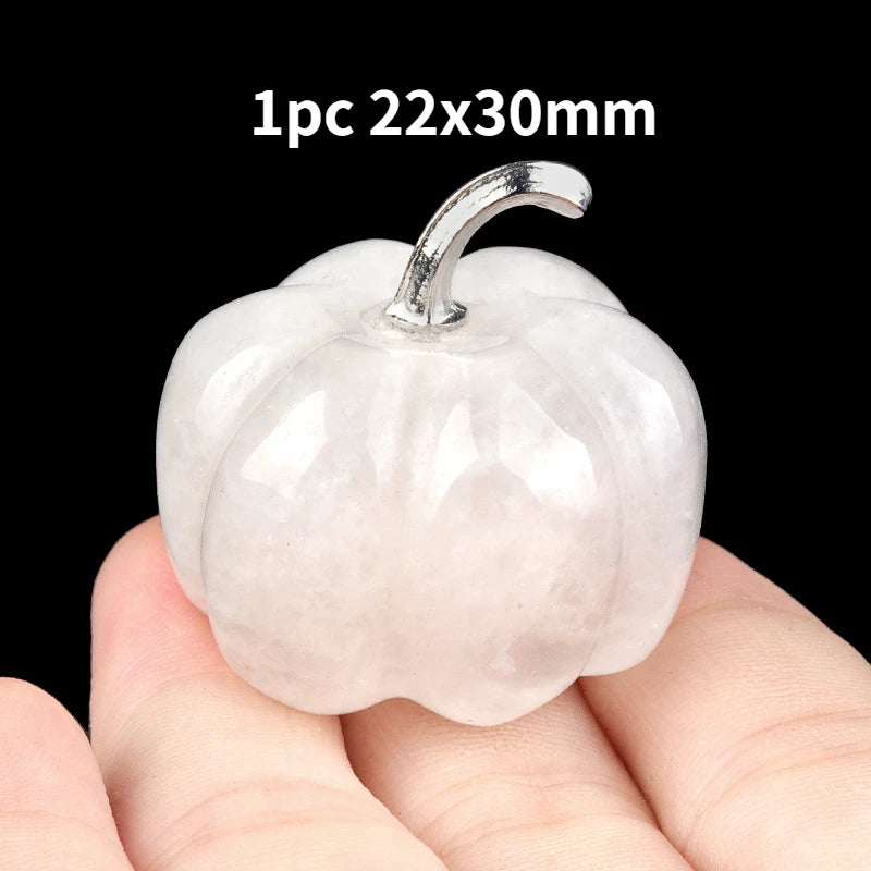 A smooth, translucent pink natural stone pumpkin figurine with a silver stem is held in a hand.