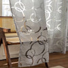 A sheer white curtain with geometric circular patterns in brown embroidery hanging indoors.