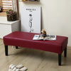 A deep red waterproof stretch dining bench cover placed on a light wood floor.