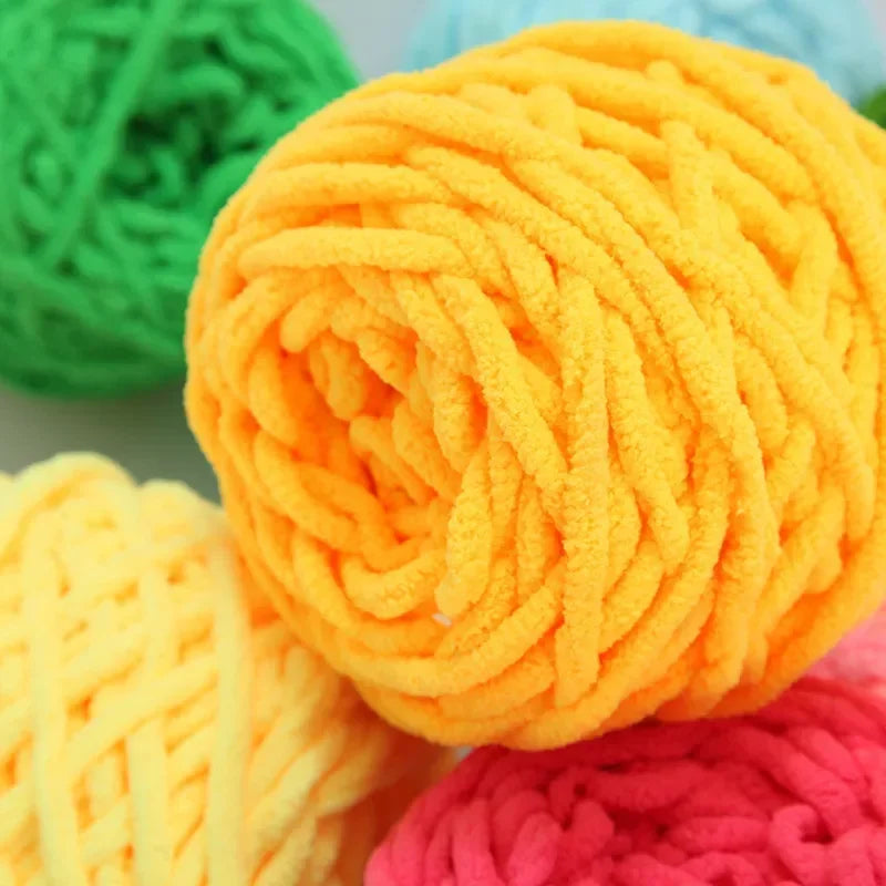 A close-up of a ball of bright orange chenille knitting yarn next to green and yellow yarn balls.
