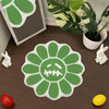 A green sunflower shaped bathroom mat with a skull design is displayed on a wooden surface next to a potted plant and small w