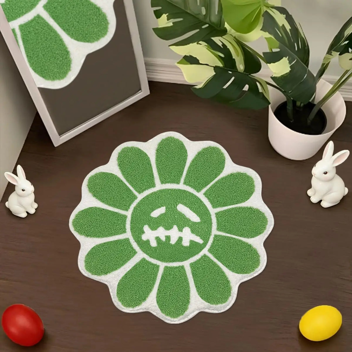 A green sunflower shaped bathroom mat with a skull design is displayed on a wooden surface next to a potted plant and small w