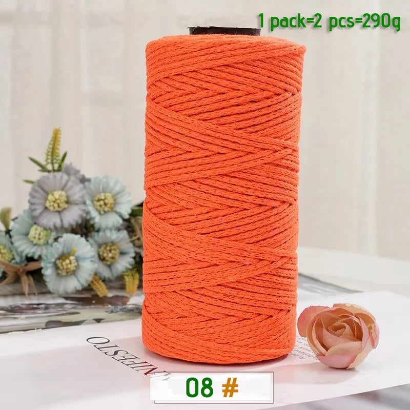 A spool of bright orange medium-thick hand-woven cotton yarn for crafting, next to a pink rose.