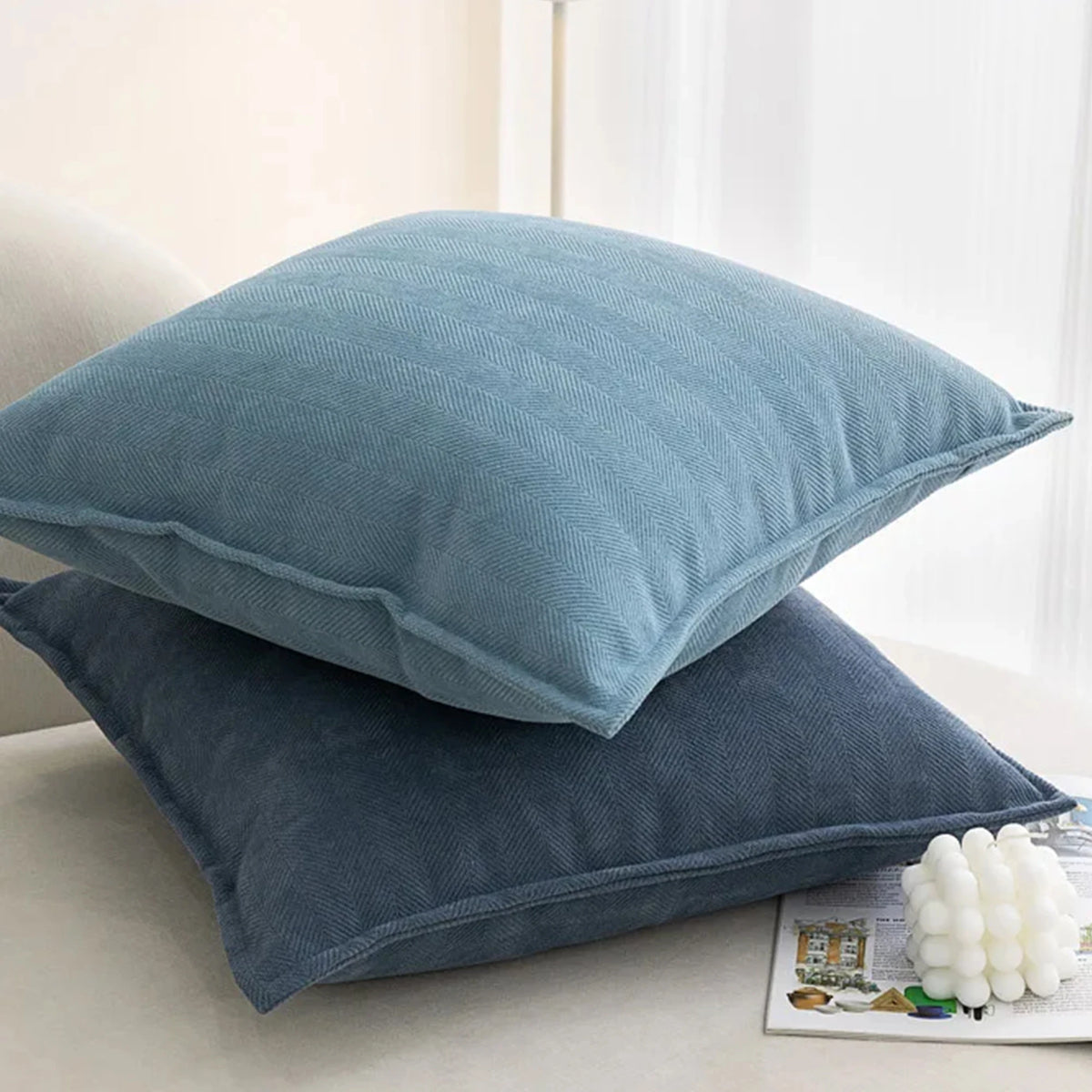 A stack of soft blue and dark blue chenille throw pillows resting on a light surface.
