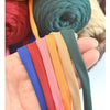 A hand holds several strands of thick polyester blended yarn in various colors including blue, red, pink, orange, beige, and 