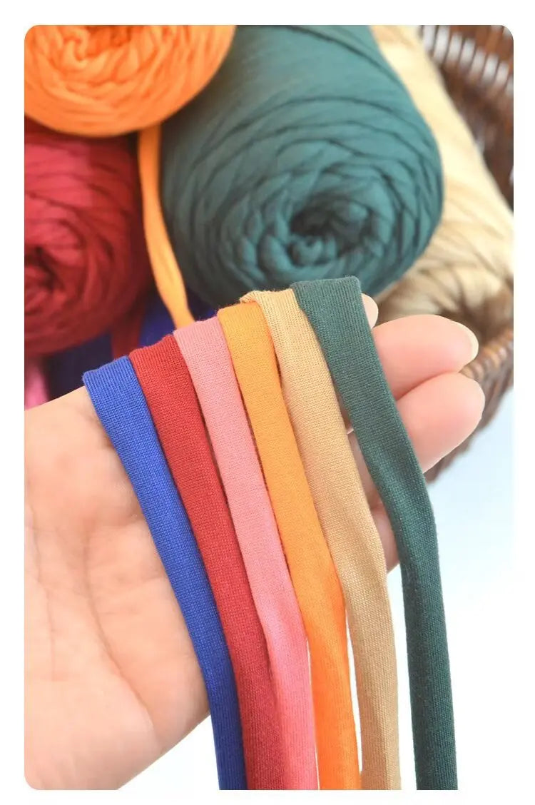 A hand holds several strands of thick polyester blended yarn in various colors including blue, red, pink, orange, beige, and 