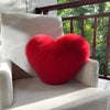 A bright red plush heart-shaped fox fur throw pillow resting on a light gray upholstered chair.