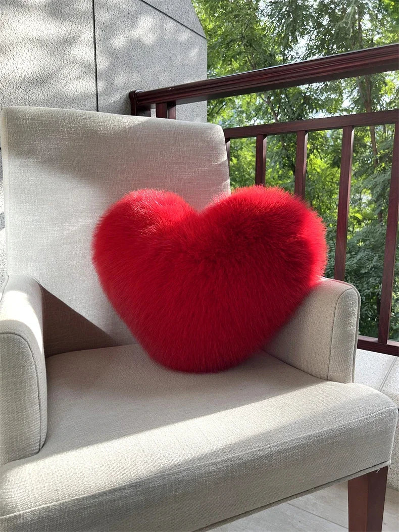 A bright red plush heart-shaped fox fur throw pillow resting on a light gray upholstered chair.