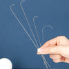A hand holds a set of thin stainless steel beading needles against a dark blue background.