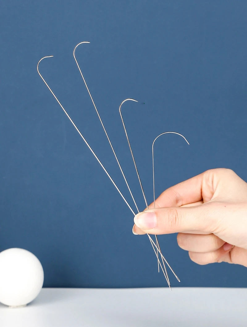 A hand holds a set of thin stainless steel beading needles against a dark blue background.