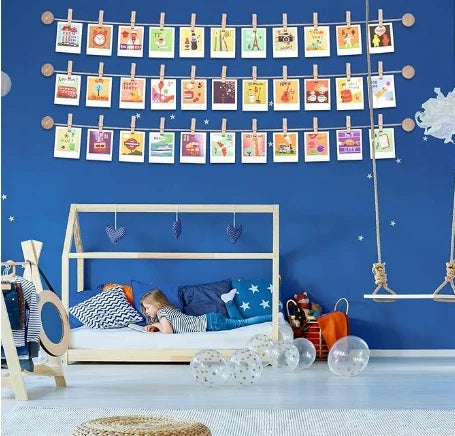 A display of small wooden clothespins with jute twine hanging against a blue wall, used for photo displays and crafts.