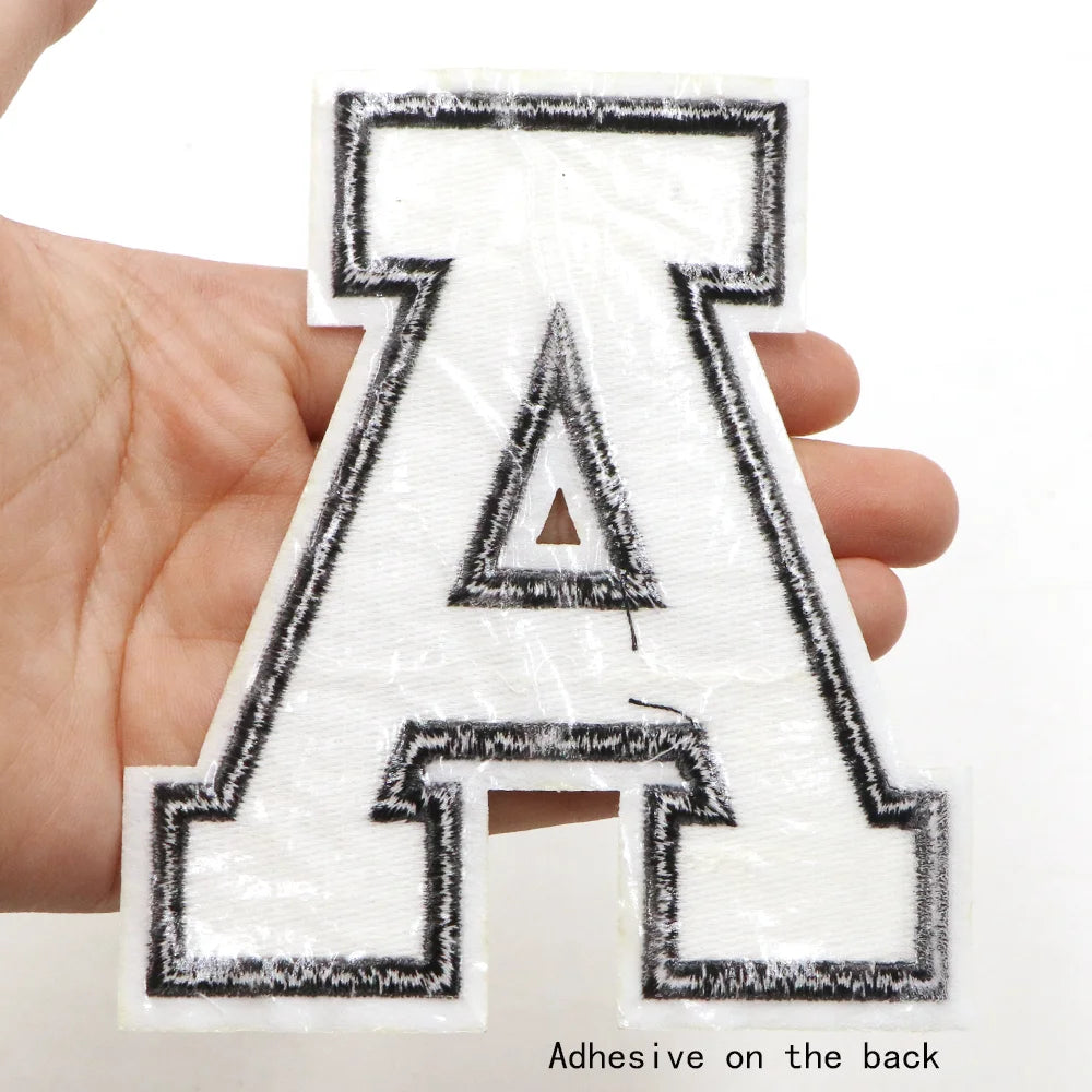 A letter patch shaped like the letter A is held in a hand, showing the adhesive on the back.
