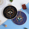 A dark embroidery hoop featuring a detailed eye design in gold and blue thread on a navy fabric.