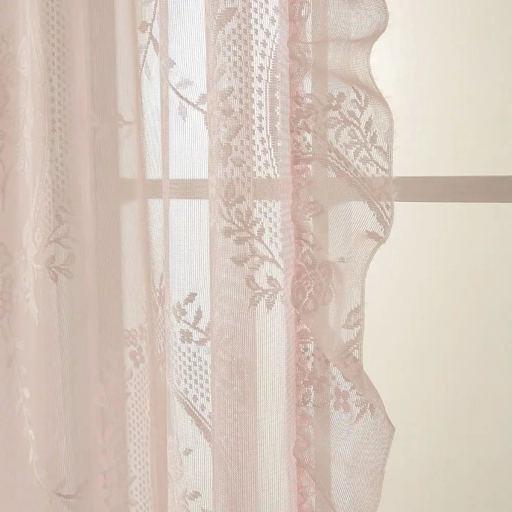 A sheer pink and white floral lace curtain set hanging in a window.