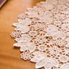 A close-up of a white floral embroidered doily or placemat with intricate lace patterns on a wooden surface.