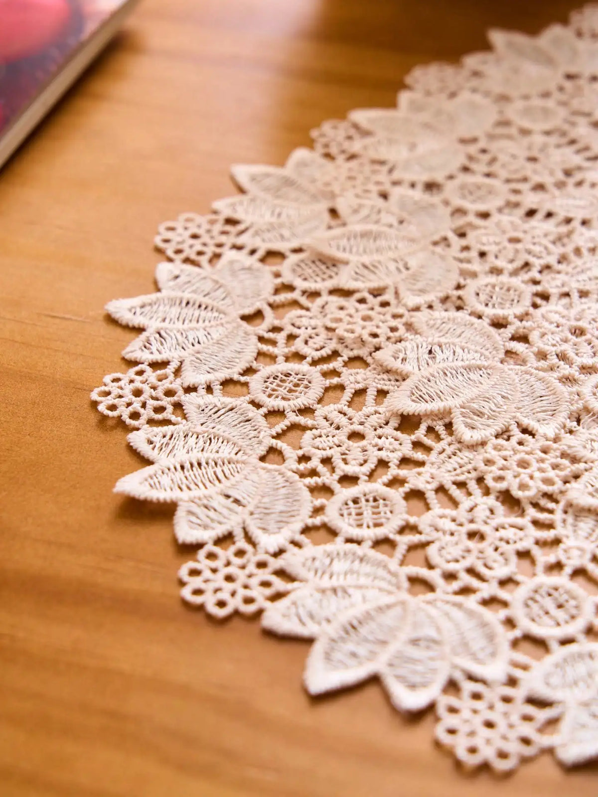 A close-up of a white floral embroidered doily or placemat with intricate lace patterns on a wooden surface.