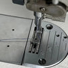Close-up view of an industrial steel presser foot with an invisible zipper being used on a sewing machine.