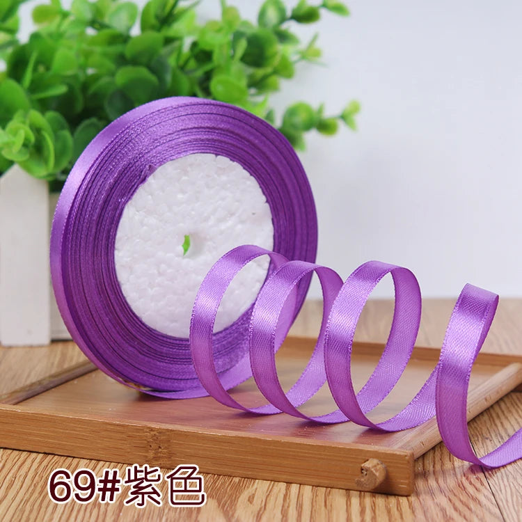 Purple satin ribbon rolled around a white candle on a wooden board.