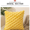 A bright yellow crystal fuzz pillow resting on a neutral textured fabric.