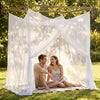 A couple sitting under a sheer white mosquito netting canopy outdoors in a grassy area.